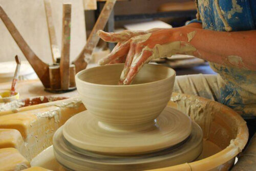 Nahaufnahme einer laufenden Töpferscheibe, auf der in der Töpferwerkstatt des Kempodium in Kempten eine Schüssel aus Ton von Hand geformt wird
