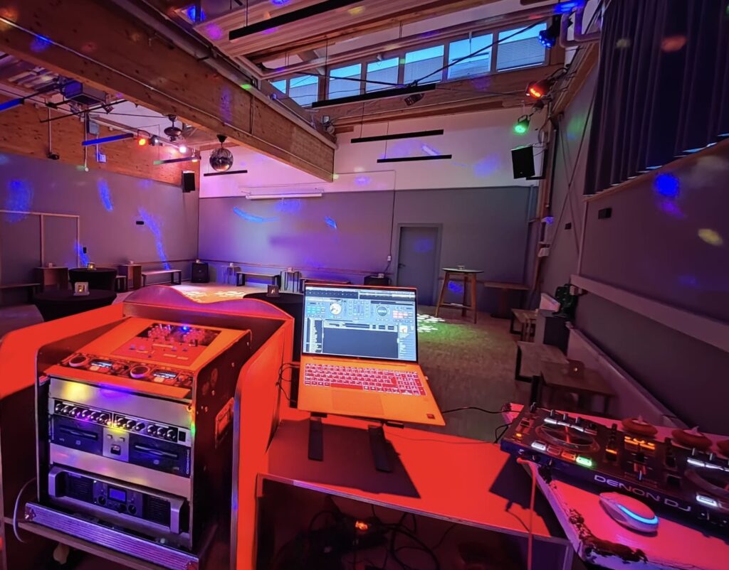 Professionelles DJ-Setup mit Laptop und Mischpult, umrahmt von bunten Partylichtern im stimmungsvollen Raum Eiche.